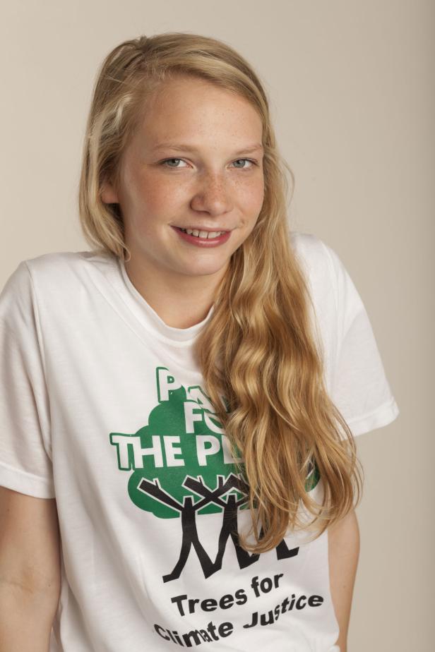 Ein junges Mädchen mit blonden Haaren trägt ein T-Shirt mit der Aufschrift „Trees for Climate Justice“.