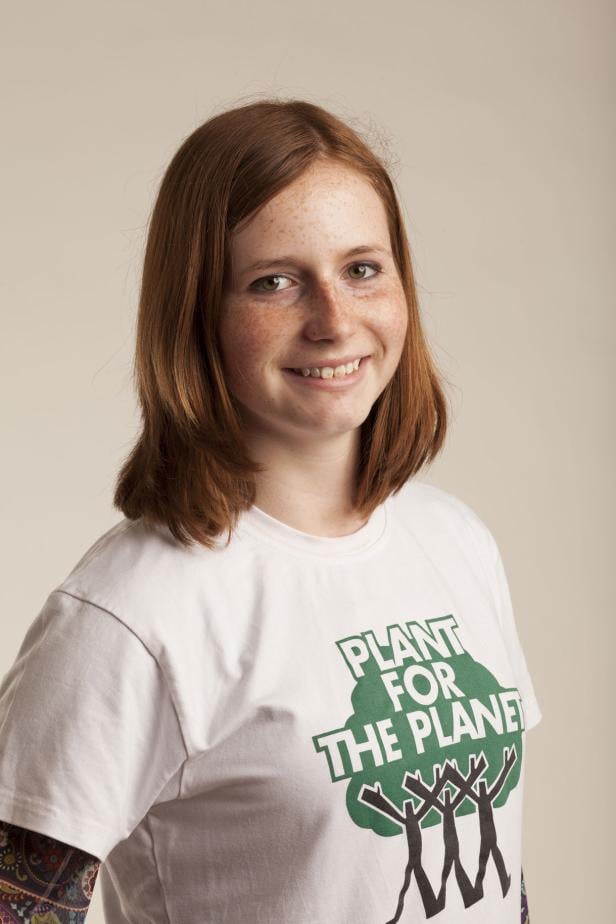 Eine lächelnde junge Frau mit roten Haaren und Sommersprossen trägt ein T-Shirt von „Plant for the Planet“.
