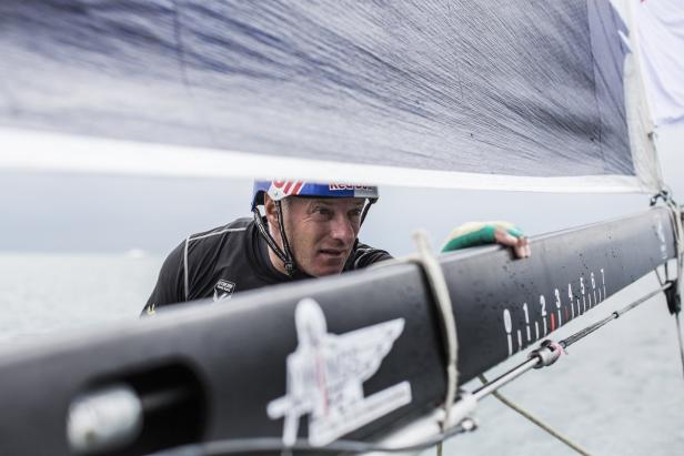 Ein Segler mit Helm und Handschuhen bedient ein Segelboot auf dem Wasser.