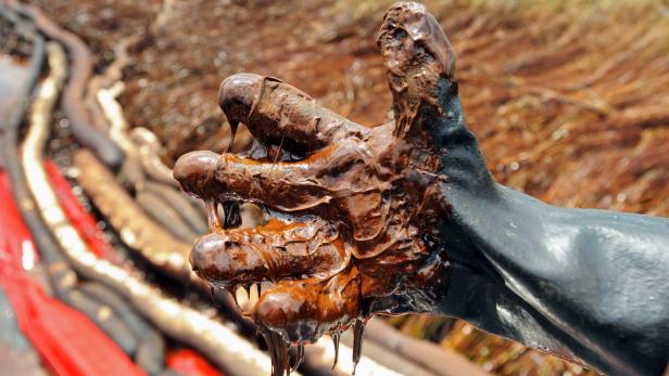 Eine Hand mit einem schwarzen Handschuh ist mit dickflüssigem Öl bedeckt.
