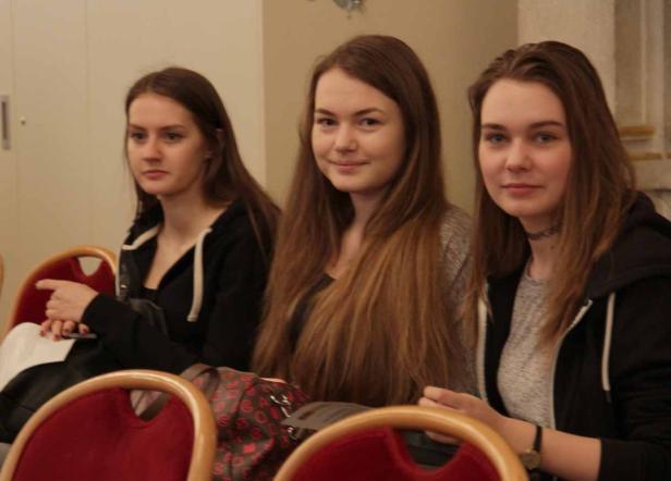 Drei junge Frauen sitzen nebeneinander auf roten Stühlen.