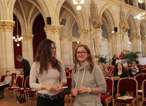 Zwei Frauen stehen in einem eleganten Saal mit roten Stühlen.