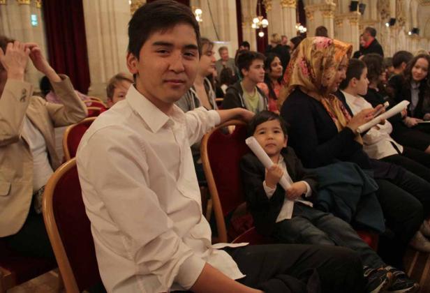 Ein junger Mann und ein kleiner Junge sitzen in einem Publikum, möglicherweise bei einer Veranstaltung.