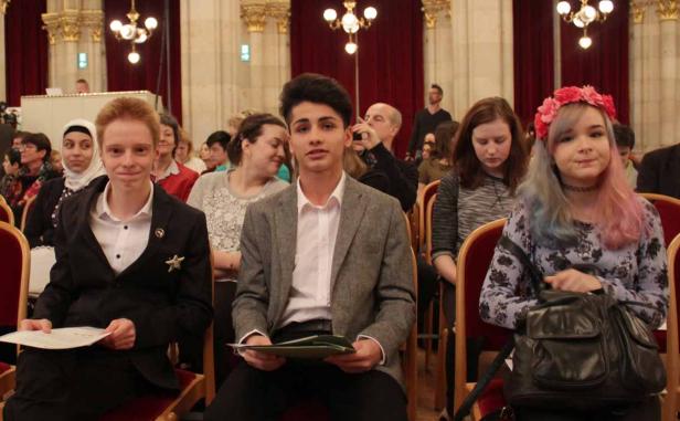 Mehrere Jugendliche sitzen in einem Saal und halten Dokumente in den Händen.