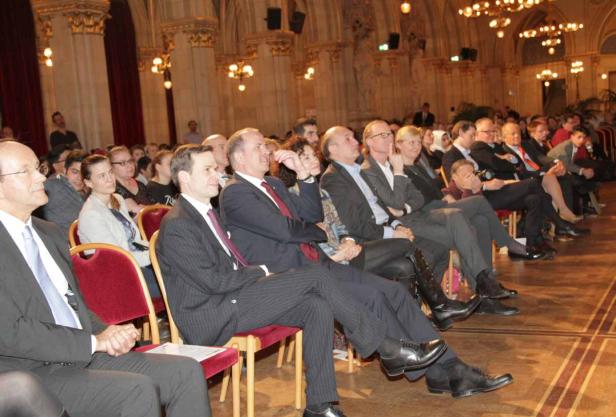 Zuschauer sitzen in einem eleganten Saal und schauen auf eine Bühne.