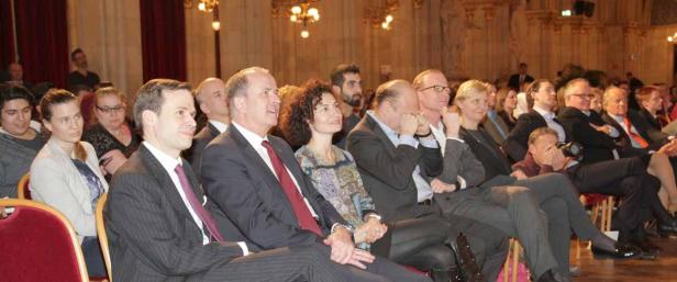 Zuschauer sitzen in einem Saal und schauen aufmerksam in Richtung Bühne.