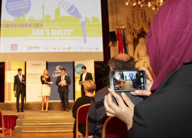 Eine Frau mit Kopftuch fotografiert eine Preisverleihung mit ihrem Smartphone.