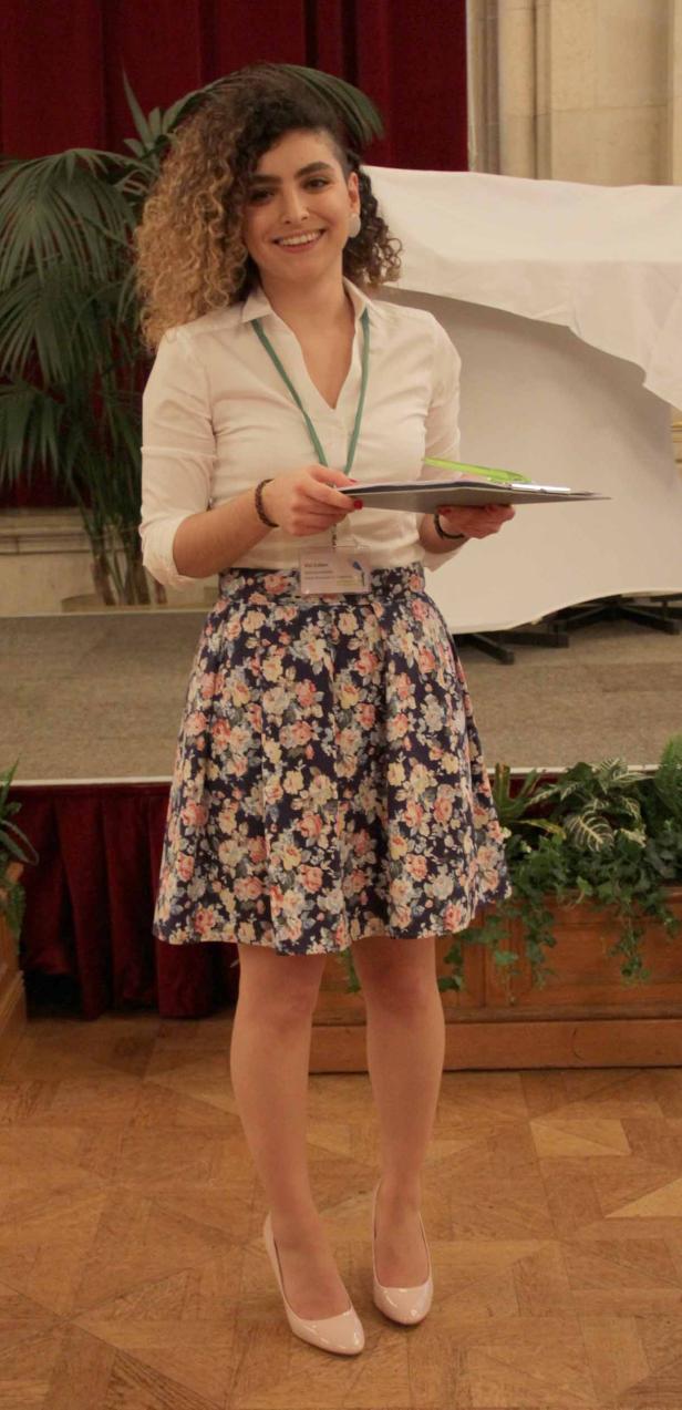 Eine Frau mit lockigem Haar und einem geblümten Rock hält ein Klemmbrett in der Hand.