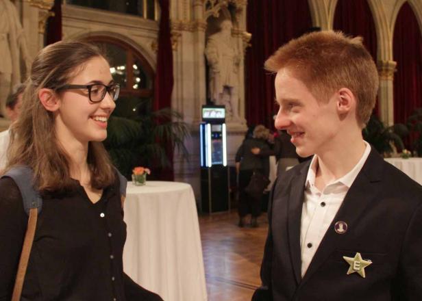 Eine junge Frau mit Brille und ein junger Mann im Anzug unterhalten sich lächelnd.