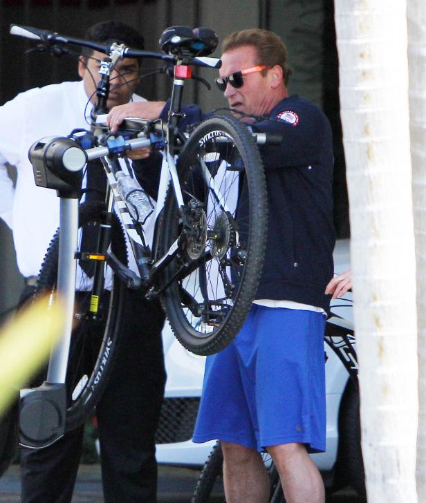 Arnold Schwarzenegger hievt ein Fahrrad von einem Fahrradträger.