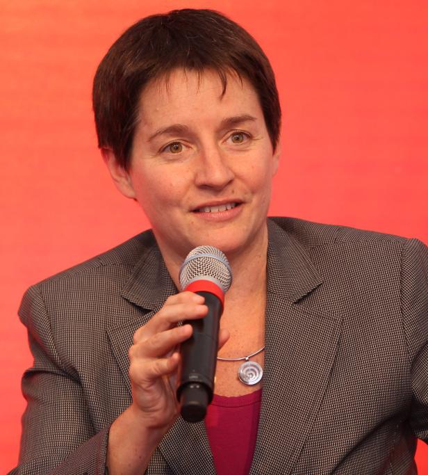 Eine Frau spricht in ein Mikrofon vor einem roten Hintergrund.