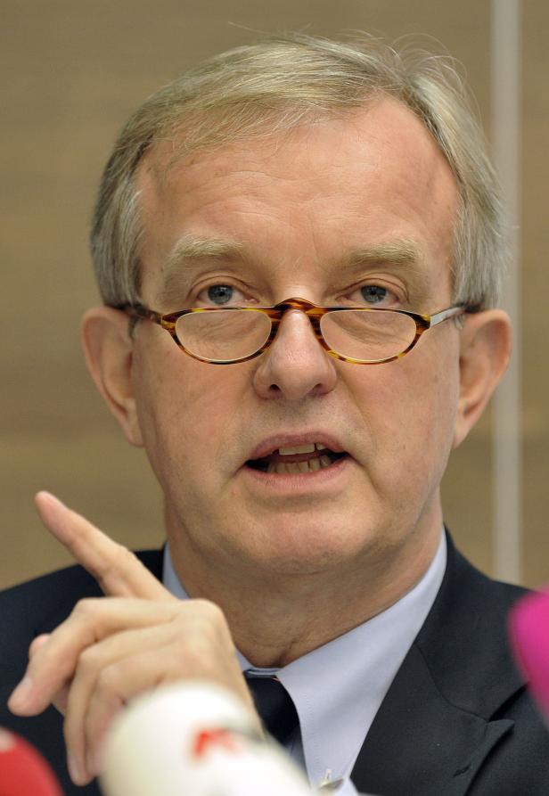 Ein Mann mit Brille gestikuliert vor Mikrofonen.