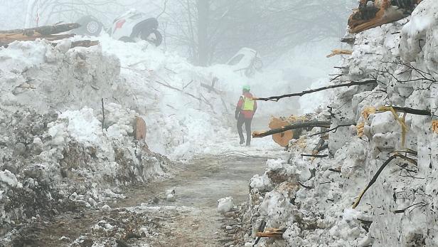 Ein Mann geht durch eine verschneite Schneise, in der auch umgestürzte Autos liegen.