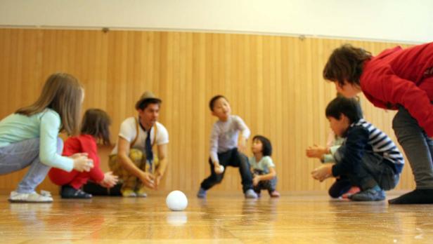 Eine Gruppe Kinder und ein Clown spielen mit einem Ball in einem Raum.