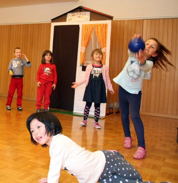 Kinder spielen vor einem kleinen Theater mit der Aufschrift „Zirkus Regenbogen“.