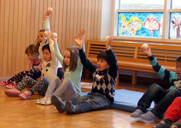 Eine Gruppe Kinder sitzt auf dem Boden und hält Bälle in die Luft.