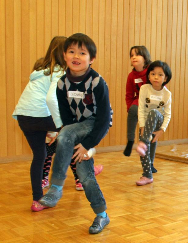 Eine Gruppe Kinder, darunter Leonard und Auitong, macht Gymnastikübungen in einem Raum.