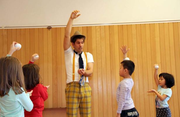 Ein Clown mit Hut jongliert mit Kindern in einem Raum.