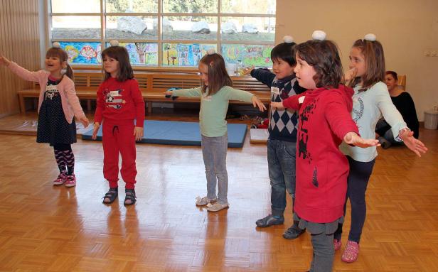 Eine Gruppe Kinder balanciert mit Gegenständen auf dem Kopf in einem Raum.