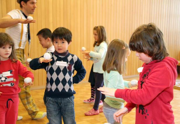 Eine Gruppe Kinder und ein Clown üben mit kleinen weißen Bällen.