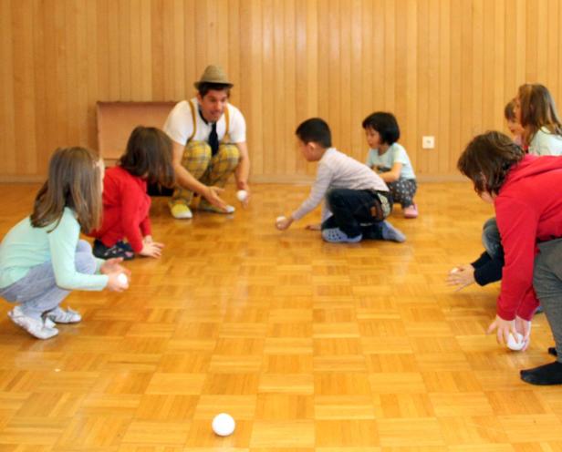 Ein Clown spielt mit einer Gruppe von Kindern auf einem Parkettboden.