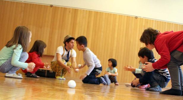 Ein Clown jongliert mit Bällen vor einer Gruppe von Kindern.