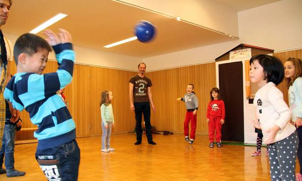 Eine Gruppe Kinder spielt mit einem Ball in einem Raum mit einer kleinen Bühne.