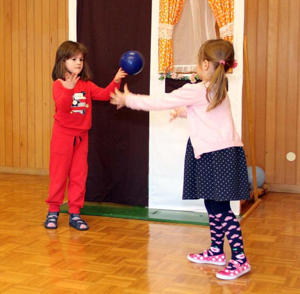Zwei Mädchen spielen mit einem blauen Ball vor einer Bühne.