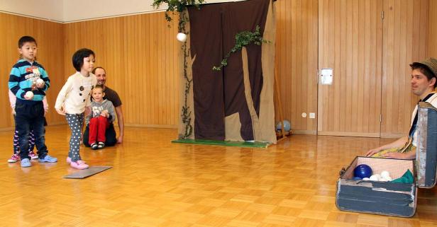 Kinder und ein Mann sitzen in einem Raum mit einer Bühnendekoration.