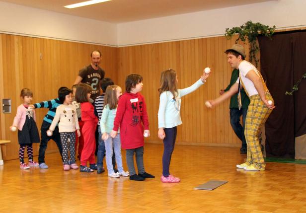 Ein Clown wirft Bälle zu einer Reihe von Kindern.