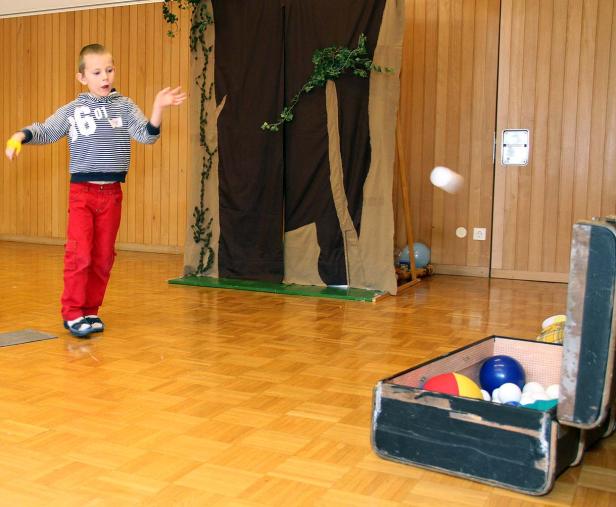 Ein Junge wirft einen Ball vor einer improvisierten Bühne mit einer offenen Truhe voller Bälle.