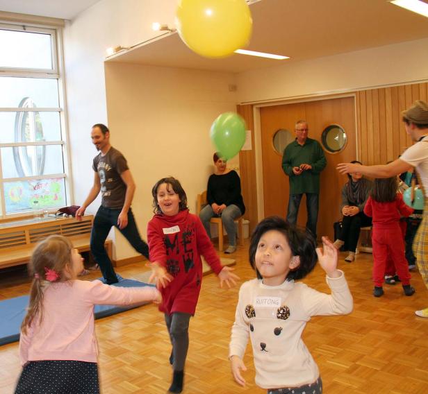 Kinder spielen mit Ballons in einem Raum, während Erwachsene zusehen.