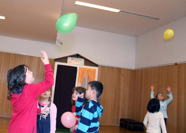 Eine Gruppe Kinder spielt mit Luftballons in einem Raum mit einer kleinen Zirkusbühne.