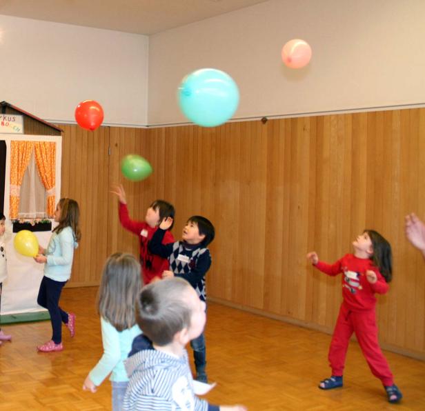 Eine Gruppe Kinder spielt mit bunten Luftballons in einem Raum.