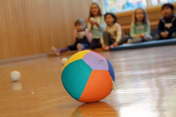 Ein bunter Ball liegt auf dem Boden, im Hintergrund sitzen Kinder.