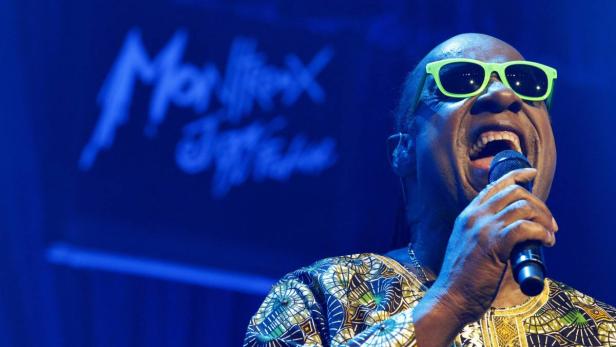 Stevie Wonder singt mit grüner Sonnenbrille auf der Bühne.