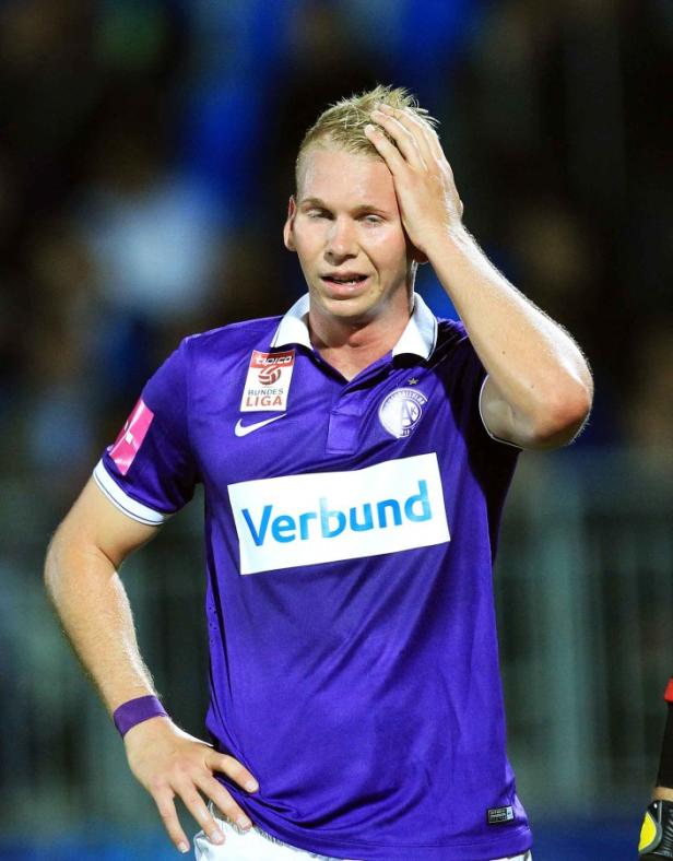 Ein Fußballspieler mit blonden Haaren in einem lila Trikot greift sich an den Kopf.