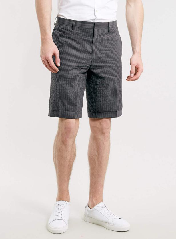 Ein Mann trägt graue Shorts mit Streifen und weiße Turnschuhe.