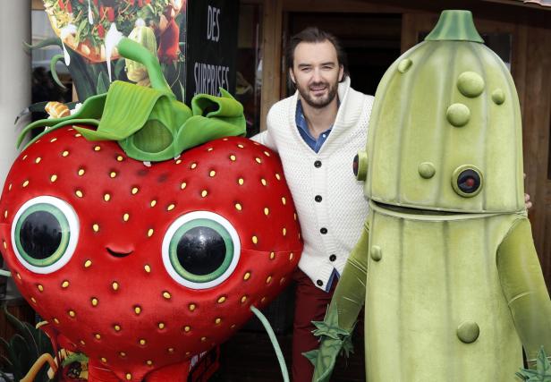 Ein Mann posiert mit Kostümen einer Erdbeere und einer Gurke.
