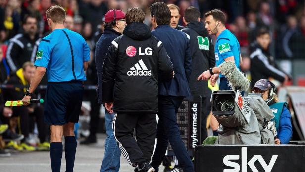 Ein Fußballspiel mit Schiedsrichtern, Trainern und einem Kameramann am Spielfeldrand.