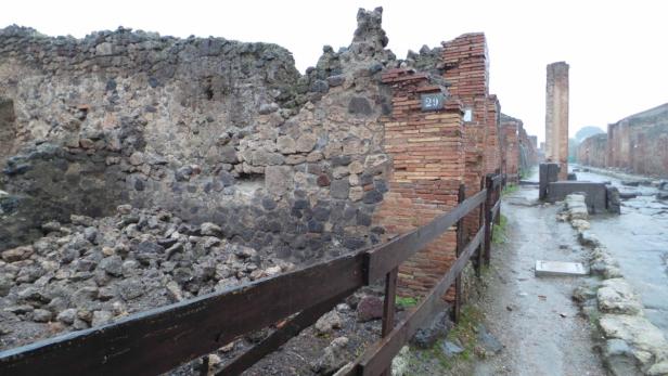 Ruinen einer antiken Stadt, möglicherweise Pompeji, mit einer hölzernen Barriere im Vordergrund.