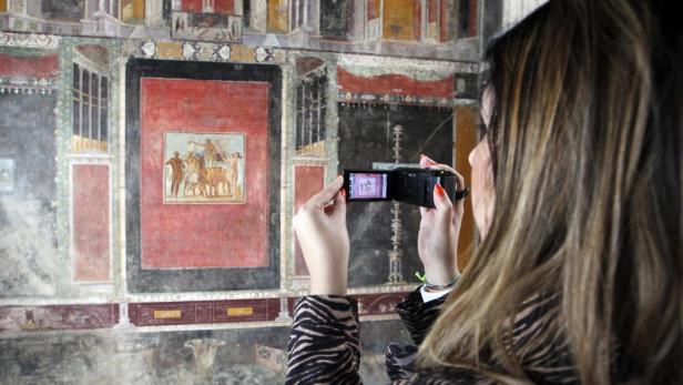 Eine Frau fotografiert ein antikes Wandgemälde mit einer kleinen Kamera.