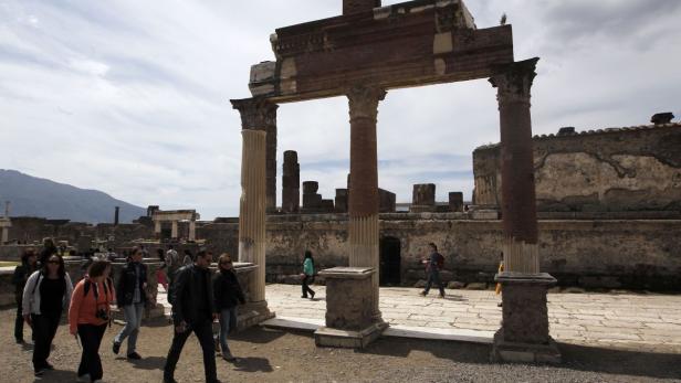 Besucher erkunden die Ruinen von Pompeji mit dem Vesuv im Hintergrund.