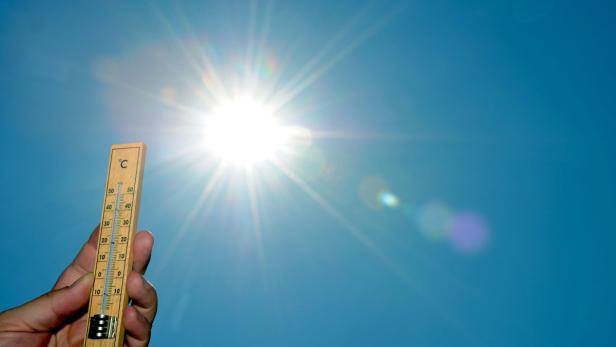 Ein Thermometer zeigt eine hohe Temperatur vor blauem Himmel und strahlender Sonne.