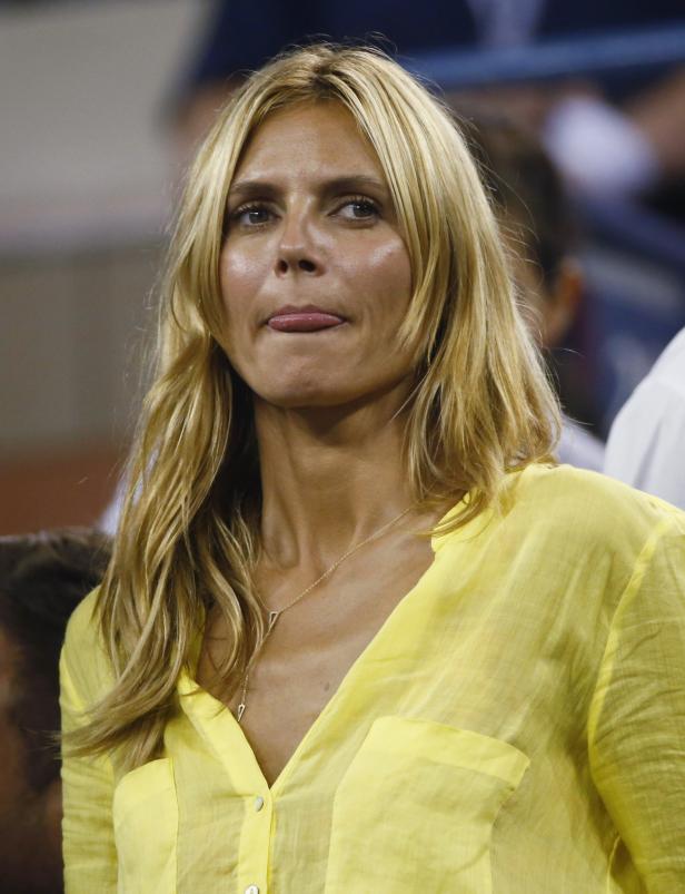 Heidi Klum in einem gelben Hemd streckt die Zunge heraus.