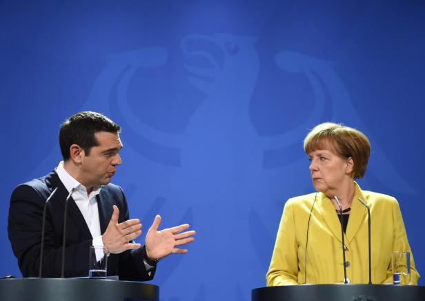 Alexis Tsipras und Angela Merkel bei einer Pressekonferenz vor einem blauen Hintergrund.