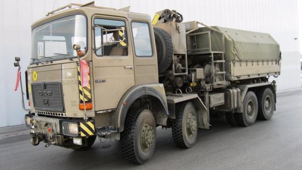 Ein olivgrüner MAN-LKW mit Plane steht auf einer asphaltierten Fläche.