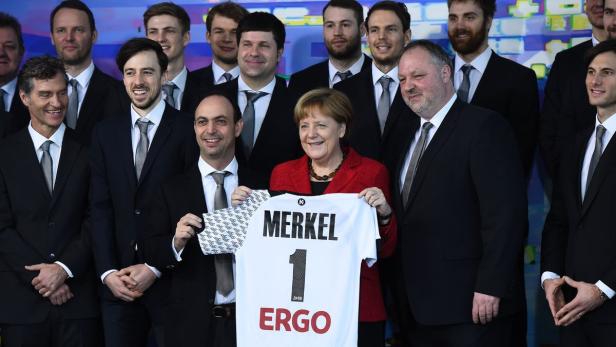 Angela Merkel hält ein Trikot mit ihrem Namen und der Nummer 1 in die Kamera.