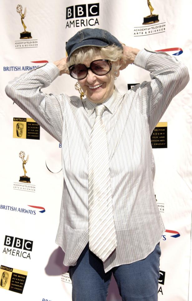 Elaine Stritch Eine ältere Frau mit Hut und übergroßer Sonnenbrille lächelt auf einem roten Teppich.