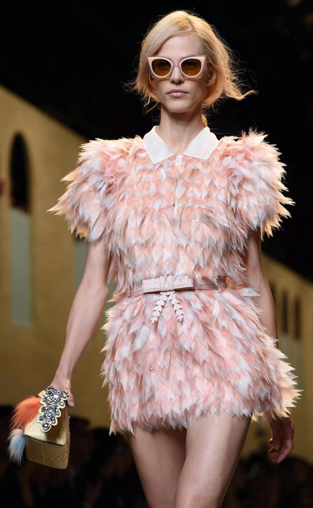 Ein Model präsentiert ein kurzes, gefiedertes Kleid mit passender Handtasche auf dem Laufsteg.